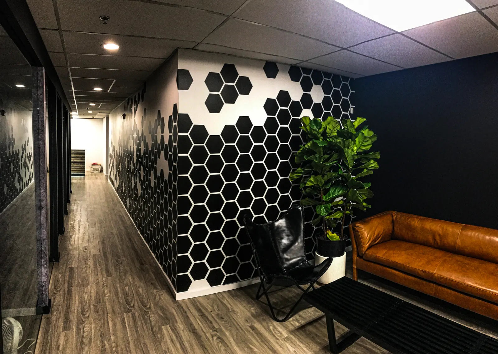 Black and white hexagon pattern wall wrap along a dark office corridor beside a leather sofa and potted plant