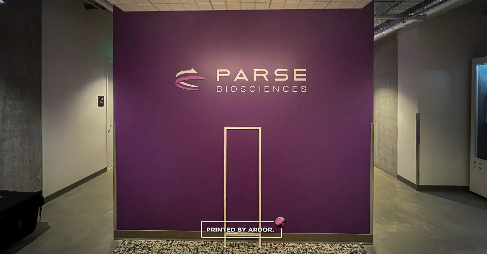 Solid purple wall wrap with the Parse Biosciences logo above a door outline, beside a concrete-floored corridor