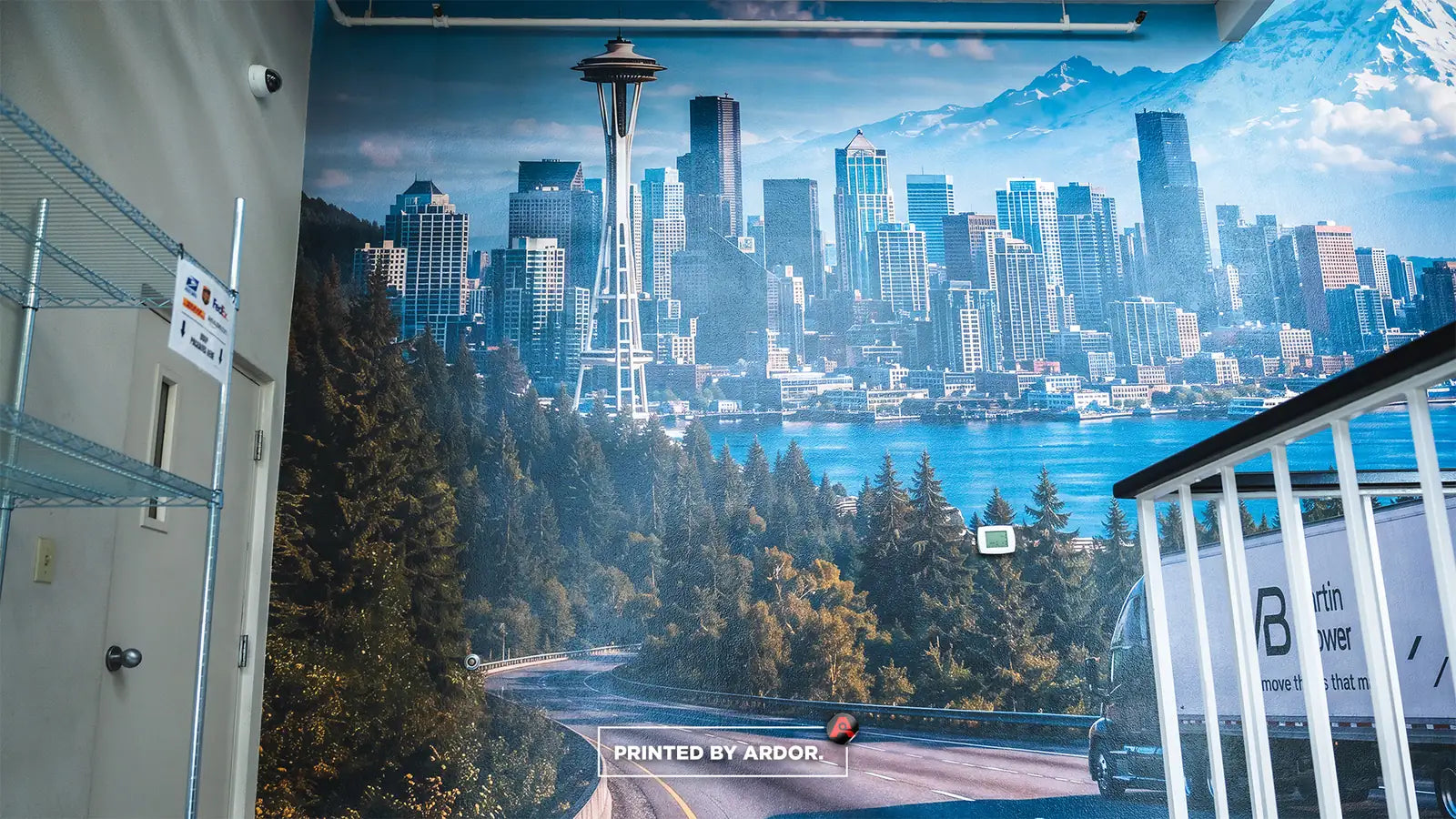 Seattle skyline and Space Needle mural with forest, lake and mountains on a wall beside metal shelving