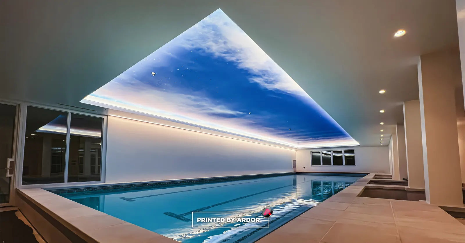 Indoor swimming pool with a ceiling wrap printed as a bright blue sky with clouds, edged with soft cove lighting