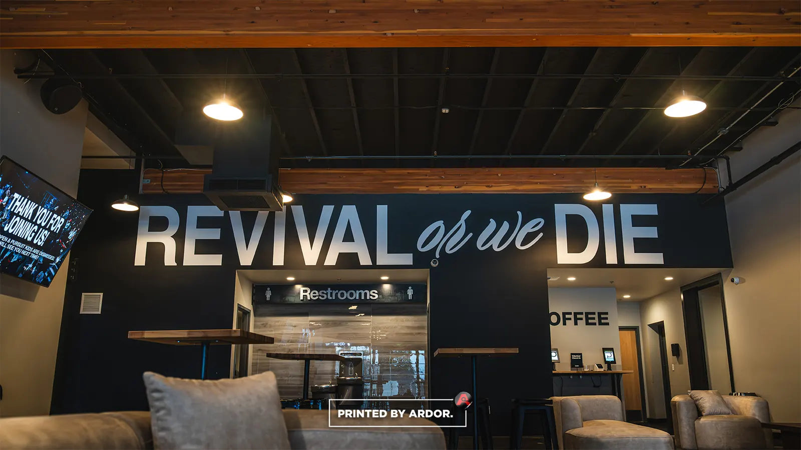 Church lobby wall with large dimensional lettering reading "Revival or we die" above the restrooms and coffee bar