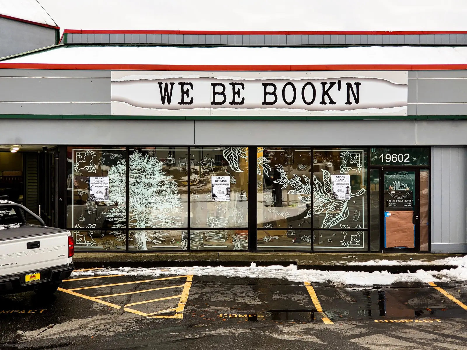 We Be Book'n storefront with white botanical window graphics of trees and leaves across the front glass, snow in the lot