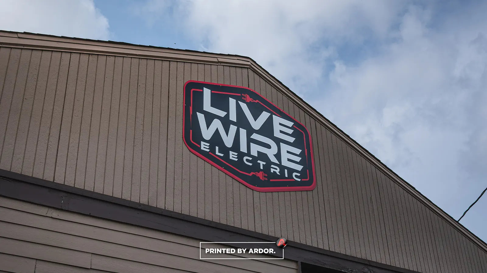 Red, black and white Live Wire Electric logo graphic applied to the wood siding of a building exterior