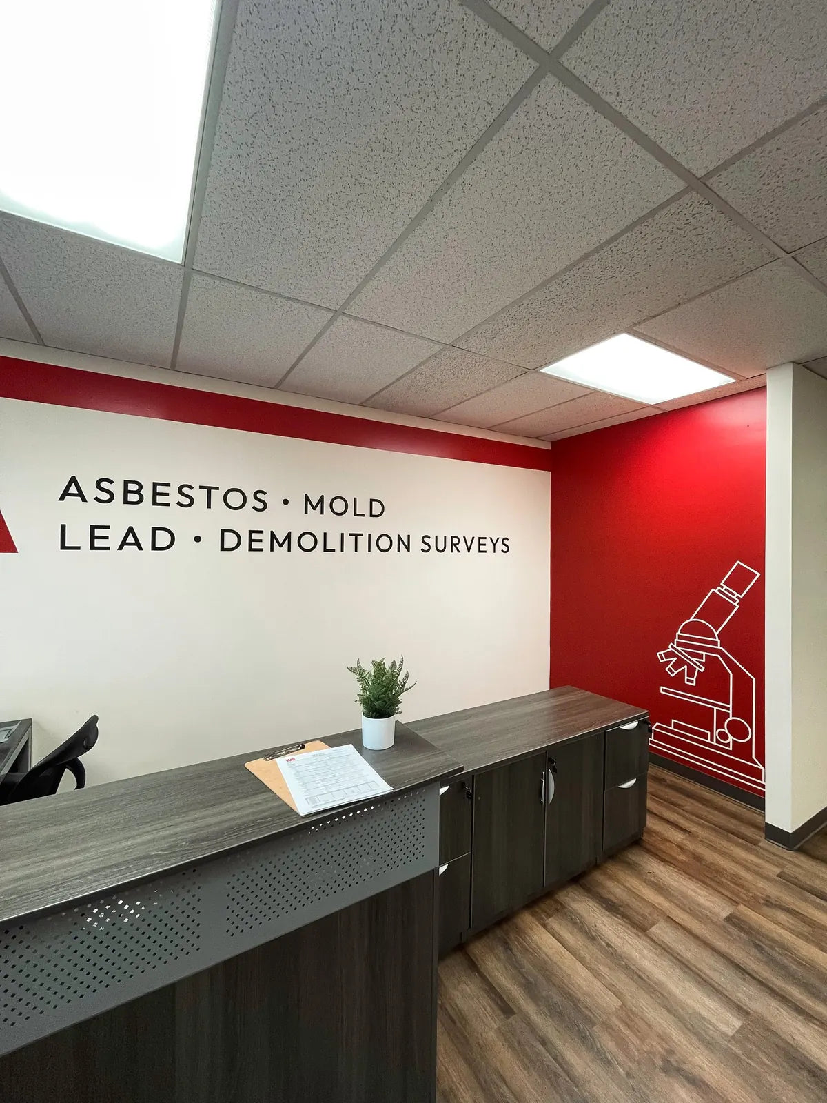 Reception area wall graphics listing asbestos, mold, lead and demolition surveys beside a red accent wall with microscope art