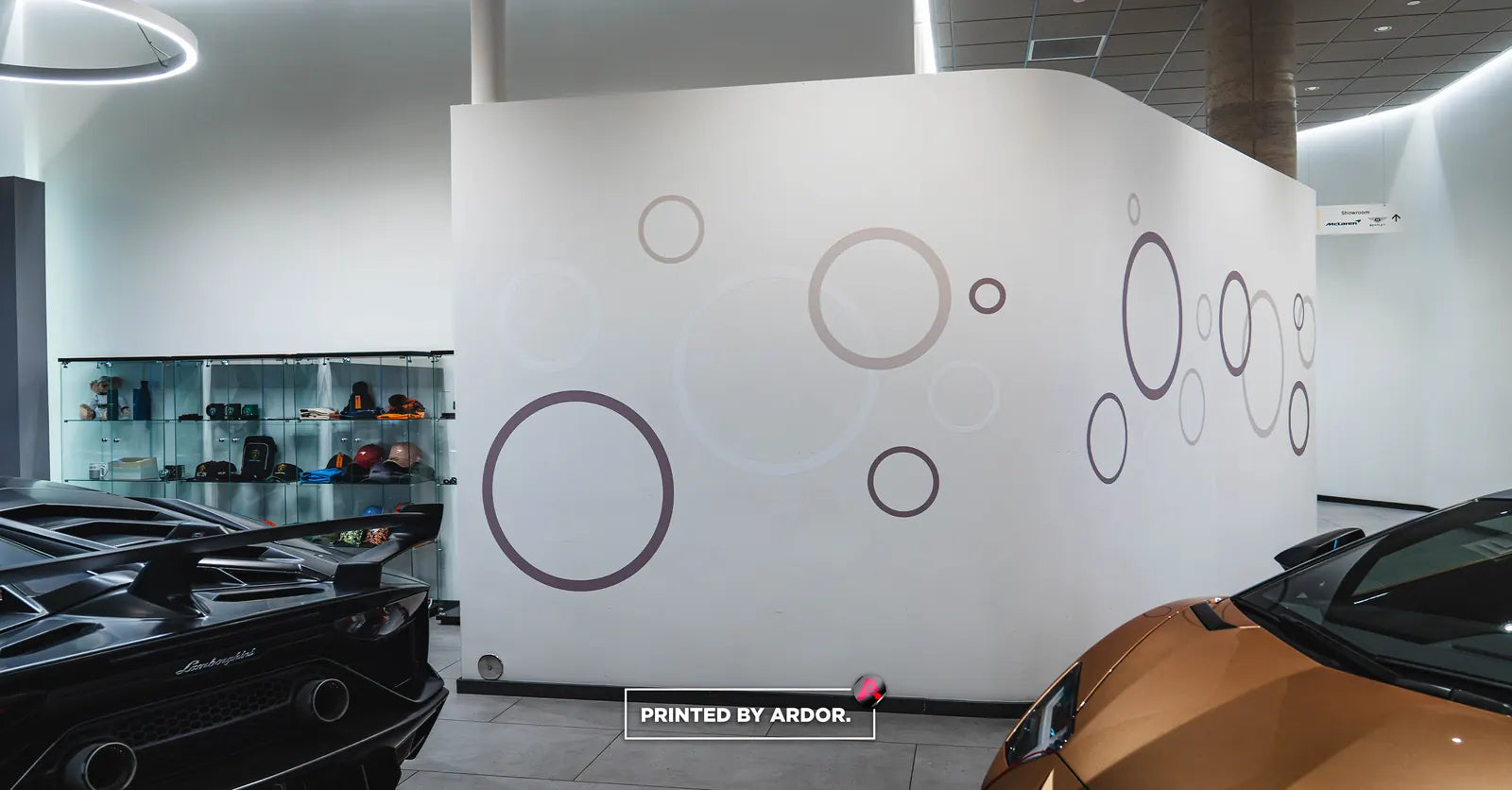 White showroom wall with subtle grey and mauve circle graphics beside two Lamborghini sports cars