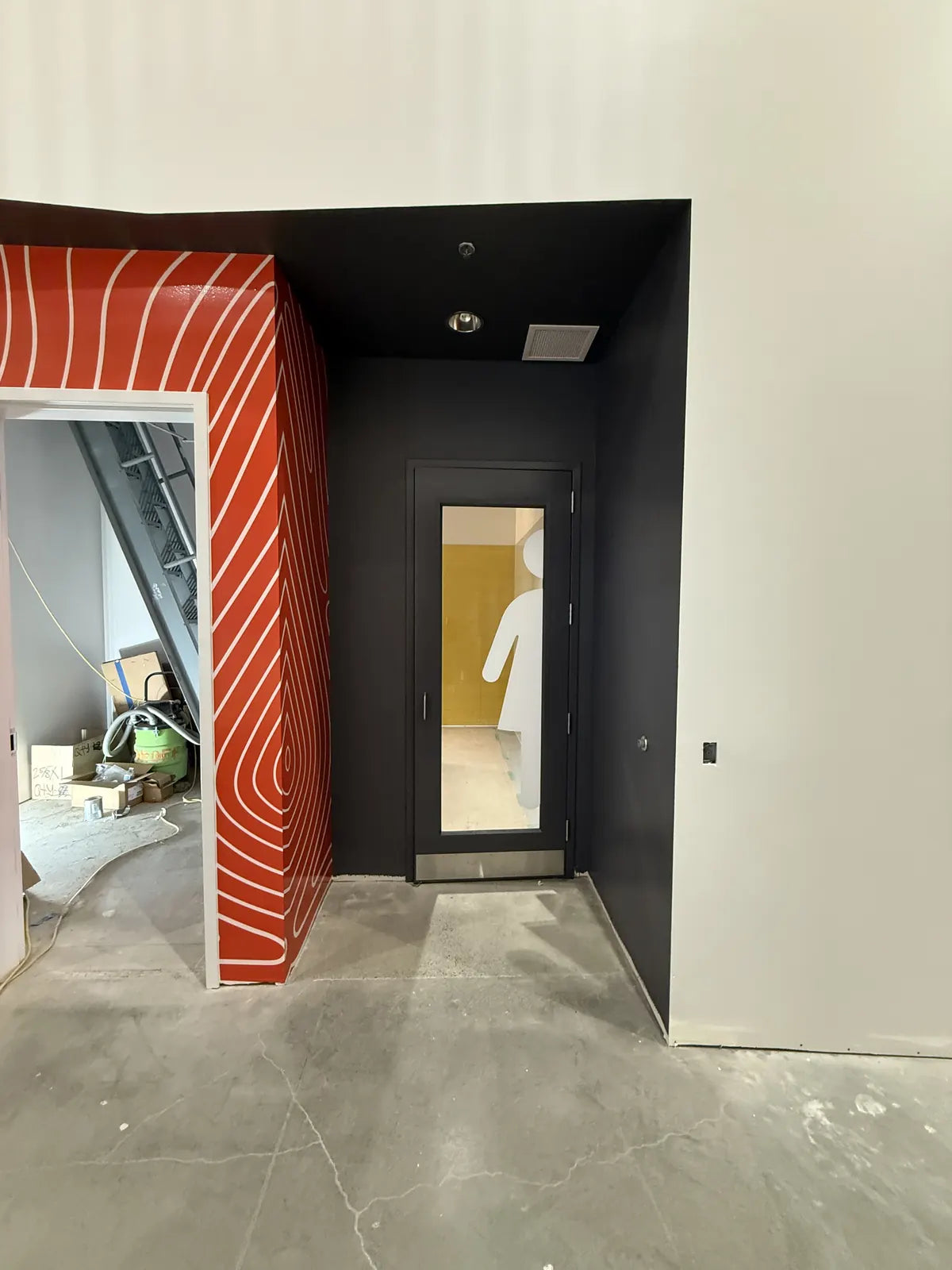 Doorway framed by a red and white swirling wave pattern wall wrap with a black surround, beside an unfinished concrete floor