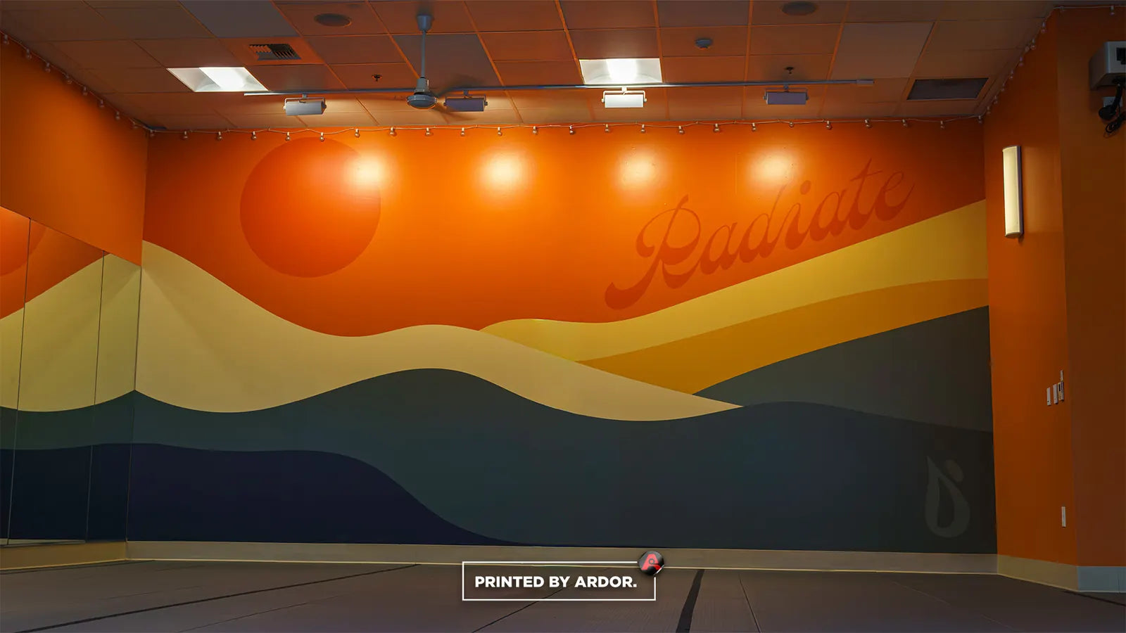 Orange and teal sunset mountain wall mural with script lettering inside the Juicy Power Yoga studio